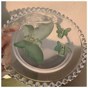 Close-up of matte green butterfly hair claw clips set on a decorative glass tray