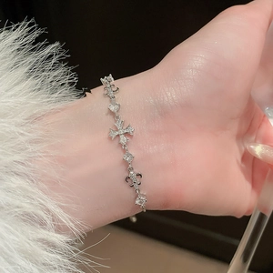 Detailed macro view of silver cross and fleur-de-lis bracelet with white zircons