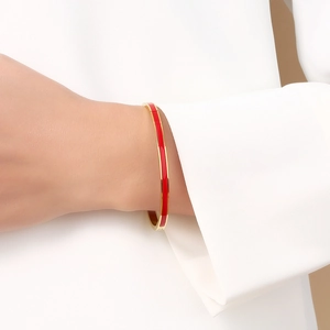 Close-up of red enamel gold-plated bangle worn by a model in a white suit