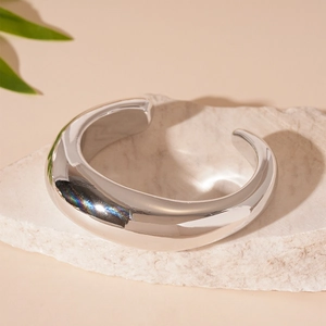 Gros plan d'un bracelet ouvert géométrique argenté posé sur une pierre naturelle blanche