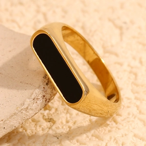 Detail view of 18K gold plated ring with a black rectangular inlay on a beige rock