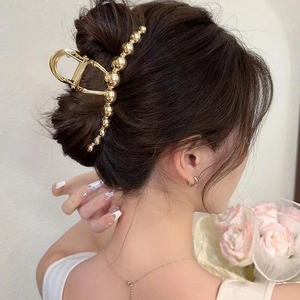 Elegant gold metal hair claw clip with bead accents shown on hair against a cream wall