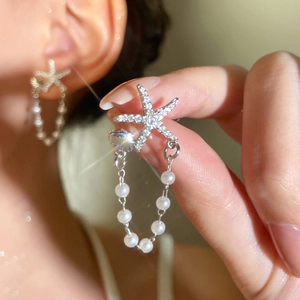 Macro shot of silver starfish earrings with rhinestones, dangling pearls and shells