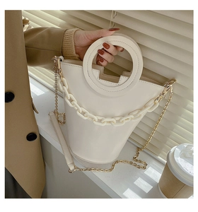 Detail of cream white bucket bag featuring ring handle, acrylic chain, and metal strap