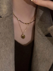 Close-up of a double-layered gold necklace with oval tiger eye stone on a wool coat