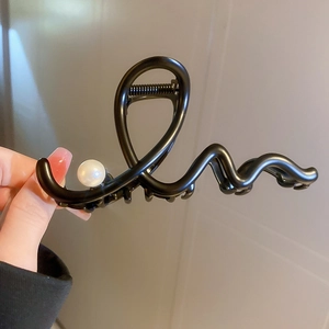 Detail of a black metal wave hair claw clip featuring a single white pearl accent