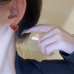Close-up of strawberry stud earrings with red glaze and gold leaves on a model ear