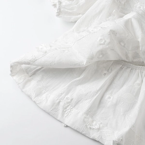 Close-up of white cotton fabric featuring intricate 3D floral embroidery details