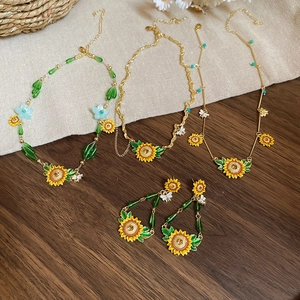 Detailed set of gold sunflower necklaces and bee earrings on rustic wood and linen