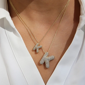 Layered gold letter K necklace with zircon pavé bubble pendants on model in white shirt