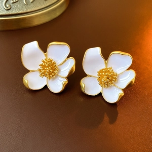 Macro shot of 3D white enamel flower earrings with golden metal edges on leather
