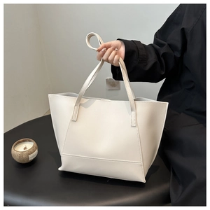 Detail of minimalist cream leather tote bag with dual handles on a black podium