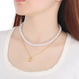 Detail of layered necklace featuring white pearls and a gold heart-shaped hollow pendant