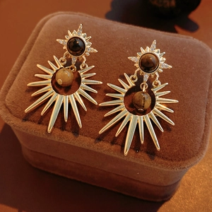 Macro detail of gold sunburst earrings with tiger eye stone and crystal accents