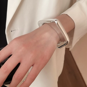 Close-up of a silver irregular geometric wide bangle on wrist over a white suit jacket