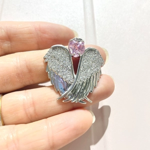 Macro detail of angel wing pendant with clear crystals and pink heart-shaped center stone