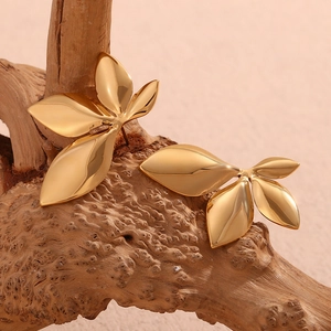 Close-up of golden leaf stud earrings on a natural wood surface with soft lighting