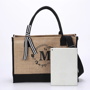 Detail of jute tote bag with black trim, striped ribbon and tablet for scale