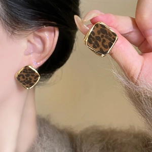 Macro view of leopard print square earrings with gold-plated edges on model's ear