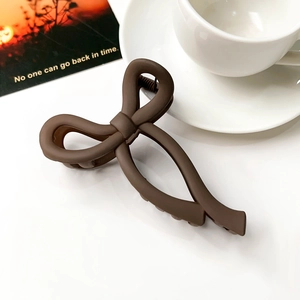 Close-up of a matte brown bow-shaped hair claw clip on a stylish aesthetic background