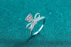 Macro shot of silver heart moissanite ring with bow design on green glitter background