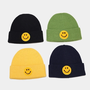 Détail de bonnets en maille de quatre couleurs avec écussons smiley jaunes brodés