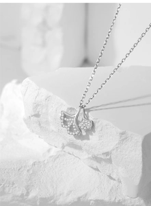 Macro shot of silver ginkgo leaf necklace pendant with white cubic zirconia pavé setting