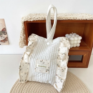 Detailed view of quilted cotton handbag featuring floral ruffled edges and small brand tag