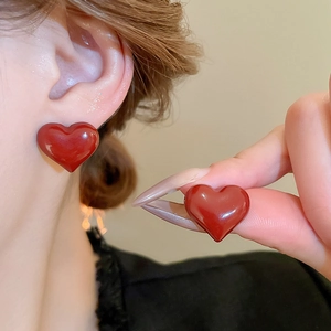 Close-up of heart-shaped red glossy stud earrings being worn to show size and scale