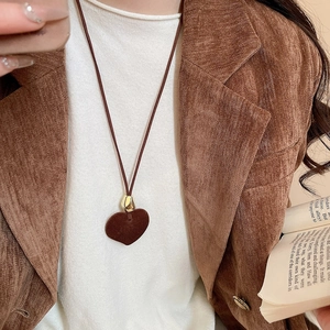 Detail of brown flocked heart pendant necklace worn over a white knit sweater