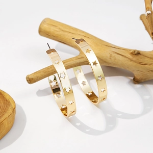 Detail of gold C-shape hoop earrings with hollow star cutouts hanging on a wood branch