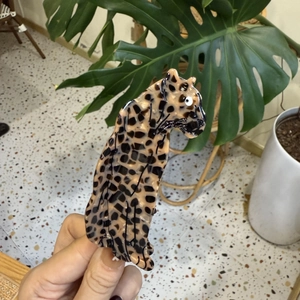 Detail showing a leopard-shaped claw clip with leopard print pattern held by hand
