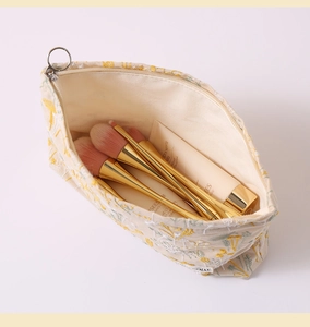 Overhead view of embroidered linen cosmetic bag with makeup brushes and skincare tubes