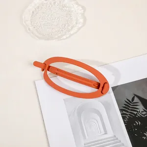 Close-up of a large matte orange oval hair claw clip on a minimalist aesthetic background