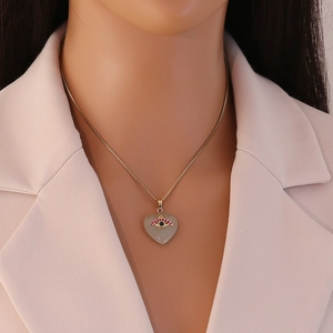 Detail of gold heart pendant necklace featuring an evil eye and pink crystals