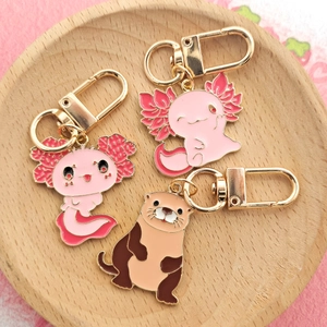 Lot de porte-clés émaillés mignons avec axolotl rose et loutre brune sur plateau bois