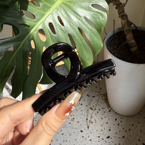 Close-up of a glossy black French claw clip held by hand in a natural home setting