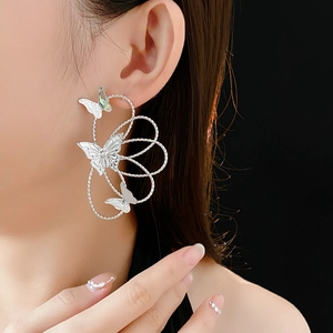 Close-up of a silver-tone hollow butterfly earring worn by a model on a black background