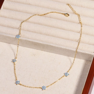 Detailed close-up of golden necklace featuring blue flower pendants and lobster clasp
