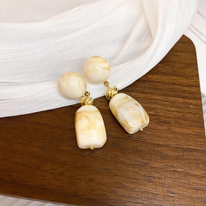 Detail of beige resin geometric earrings with marble texture and gold metal accents