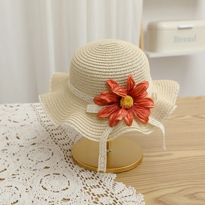 Détail d'un chapeau de paille beige avec bordure en dentelle et une fleur orange vif