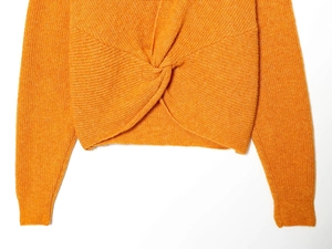Detailed view of the twist knot design and fine knit texture on an orange sweater