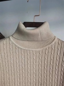 Dettaglio del maglione beige a collo alto con trama intrecciata e motivo a trecce
