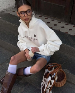 Detail of half-zip collar and retro crest print on cream oversized sweatshirt
