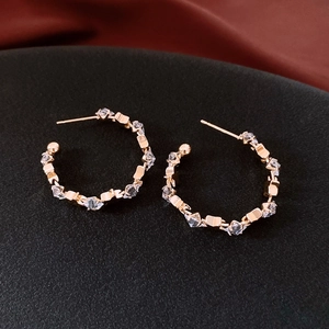Macro shot of gold C-shaped earrings with sparkling cubic zirconia on black fabric