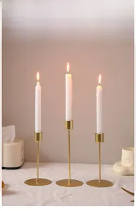 Detailed view of three gold iron candlesticks with slim white candles on a dining table