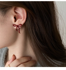 Close-up of red bow stud earrings showing smooth lacquer finish and gold pin on model ear