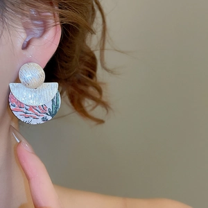 Détail de boucles d'oreilles rondes en bois avec imprimé désert et disques argentés