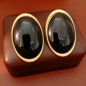 Detail of vintage oval black resin earrings with a gold matte metal frame on leather