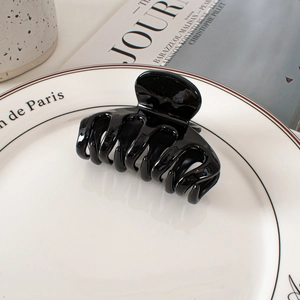 Close-up of a glossy black minimalist hair claw clip on a white ceramic display plate